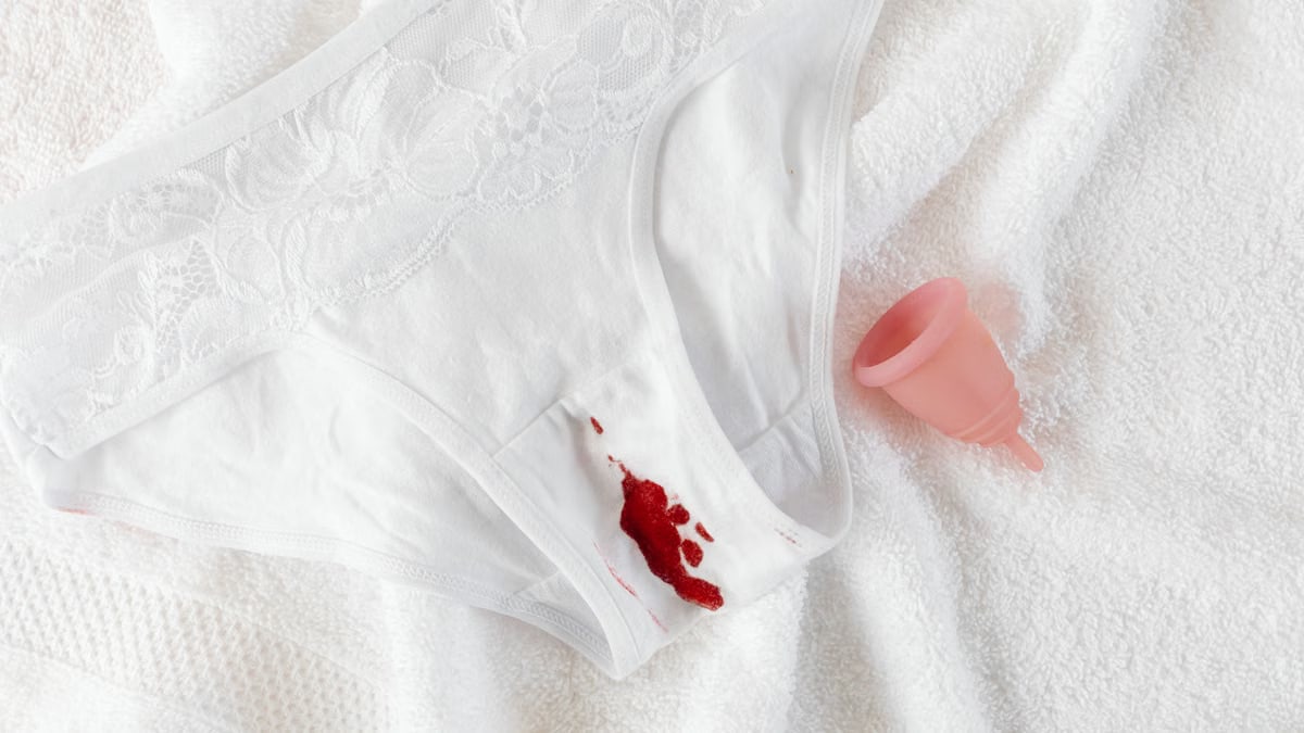 A menstrual cup alongside stained underwear on a clean towel, symbolizing menstrual health.